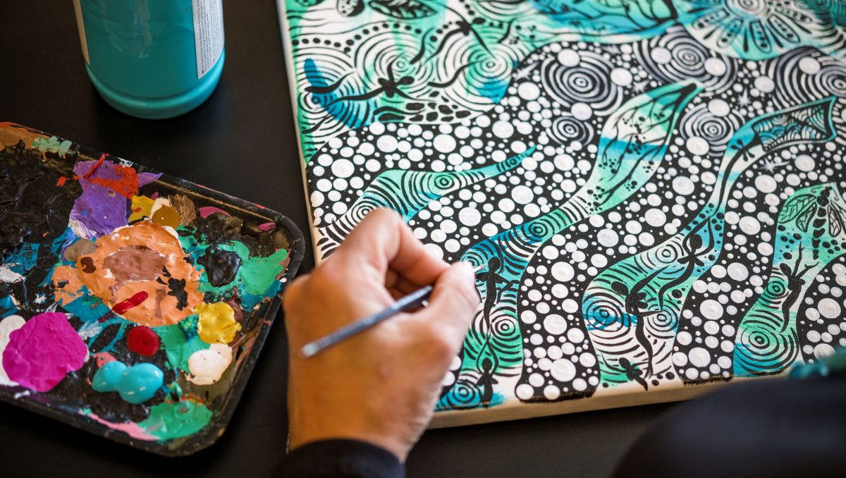 A hand working on an Indigenous art pieces