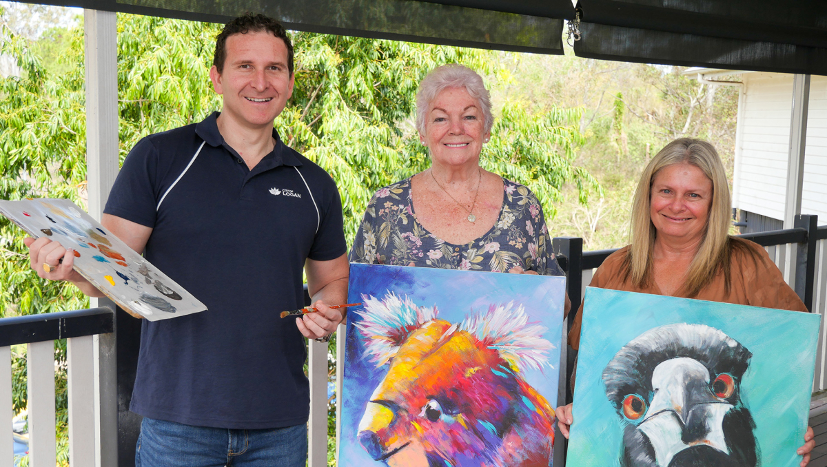 Lifestyle Chair Councillor Tony Hall previews the paint and sip sessions offered by Logan Artists Association’s Di Flack (centre) and Kristy Flynn (right) at this year’s Logan Seniors Big Day Out.