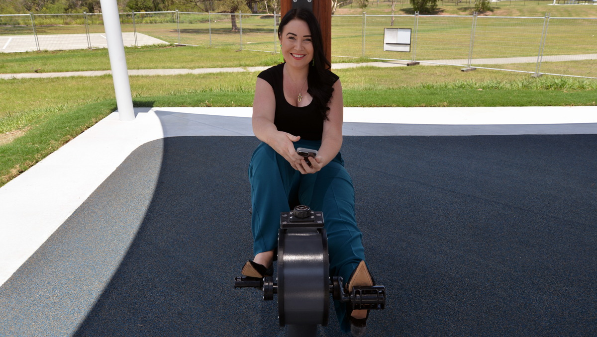 An image of Cr Mindy Russell trying out the new exercise equipment in Mabel Park, which includes a stationary bike that also charges your phone.