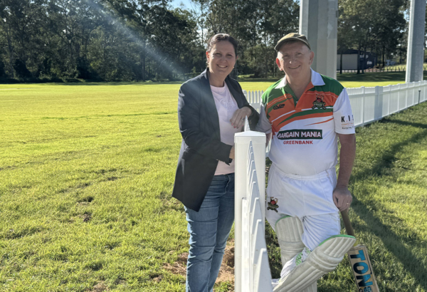 An image of Cr Natalie Willcocks and Greenbank Cricket Club president Shane Harris chatting across the club’s new eye-catching white picket boundary fence.