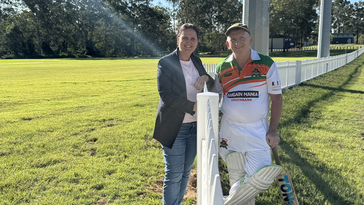 An image of Cr Natalie Willcocks and Greenbank Cricket Club president Shane Harris chatting across the club’s new eye-catching white picket boundary fence.
