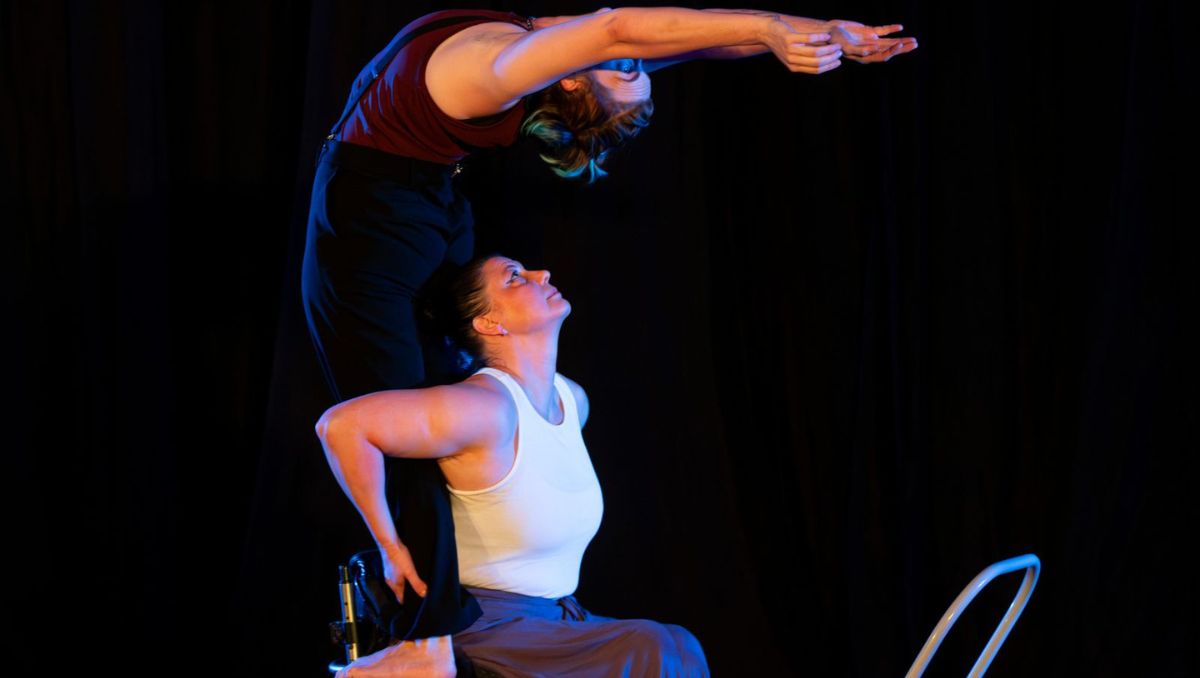 Woman in wheelchair holds feet of woman bending backwards over the wheelchair